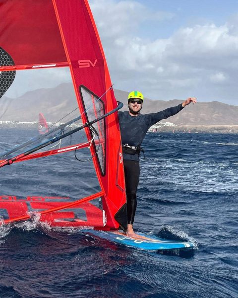 mateus isaac em cima da vela no mar sorrindo e com braço esticado