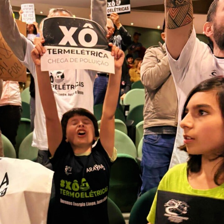 Criança segurando cartaz escrito 'Xô termelétrica' em audiência pública sobre instalação em Caçapava; evento em SJC foi suspenso mais uma evz