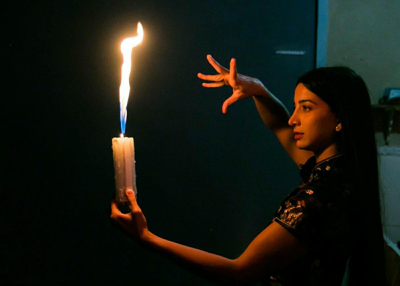 cena de filme de terror em que garota segura vela acesa e faz gesto de magia com a outra mão