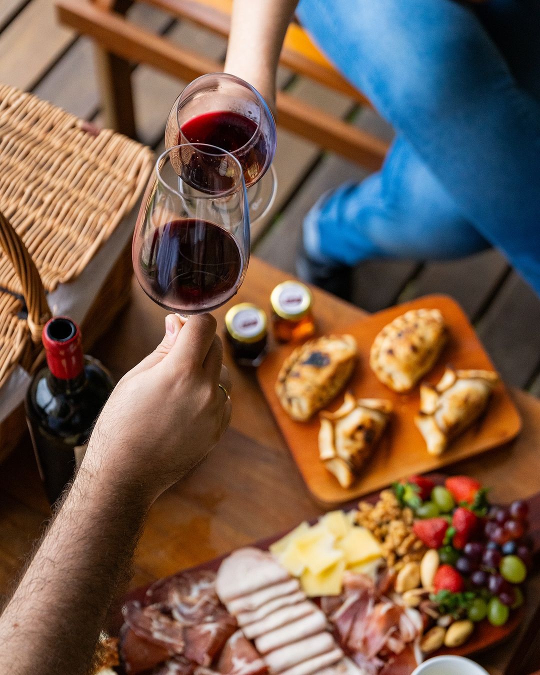 foto top view de mesa com tábuade frios, empanadas e pessoas brindando com taças de vinho