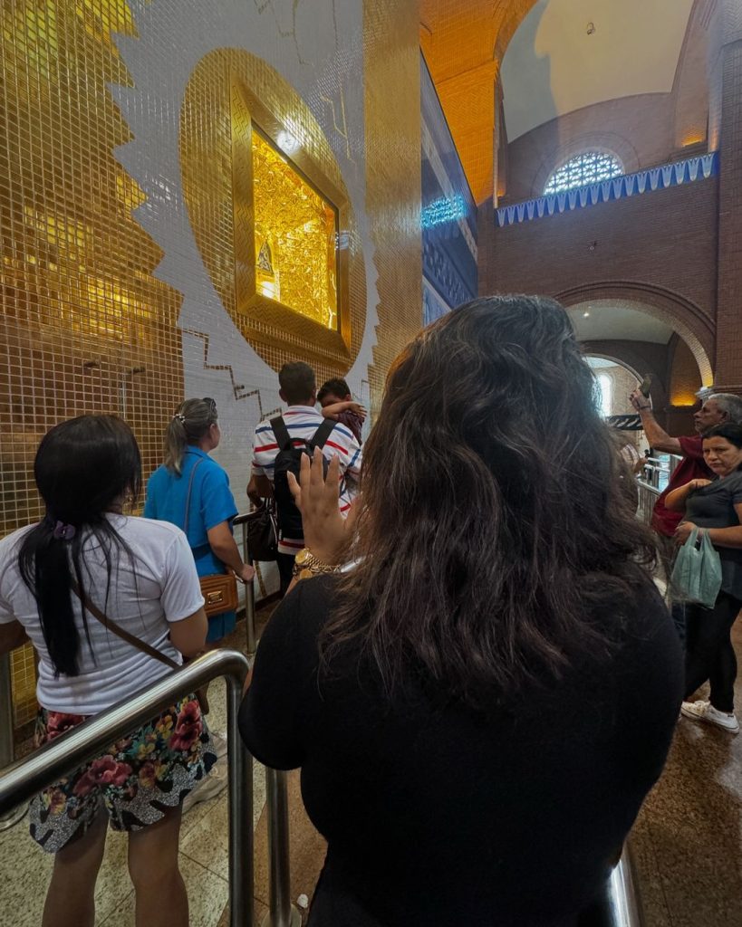 Preta Gil em visita ao Santuário Nacional de Aparecida; ela ergue as mãos em frente à Santa