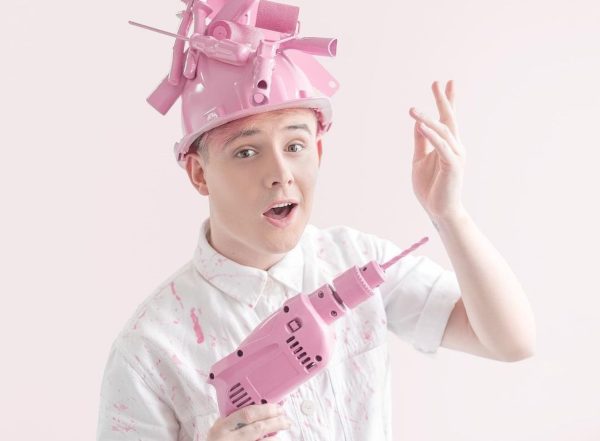 Matheus Ilt segurando furadeira rosa e com chapéu de construção cheio de ferramentas rosas coladas