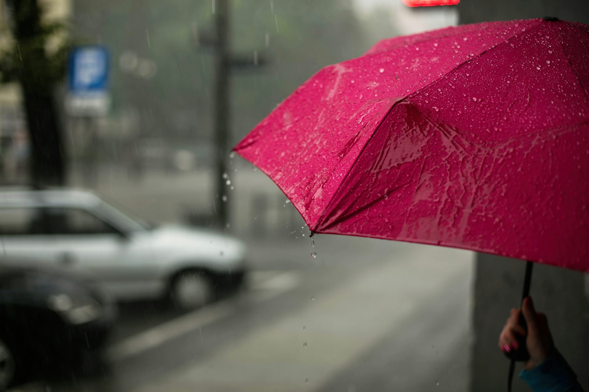 mulher segurando um guarda-chuva rosa na rua em dia nublado com pancada de chuva