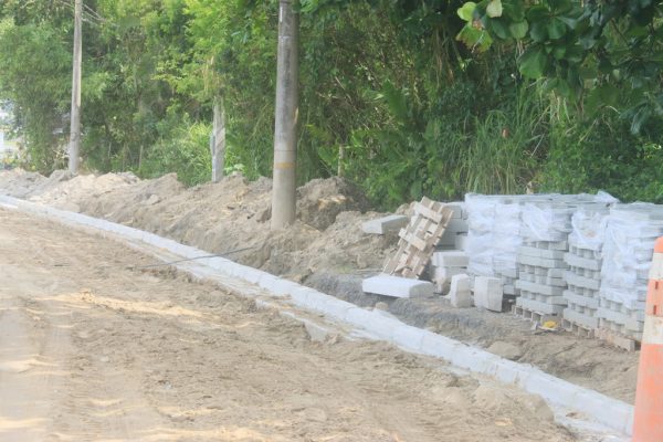 Trecho da rua de acesso ao Molhe Norte do Rio Juqueriquerê sem pavimentação com os bloquetes empilhados na lateral da via