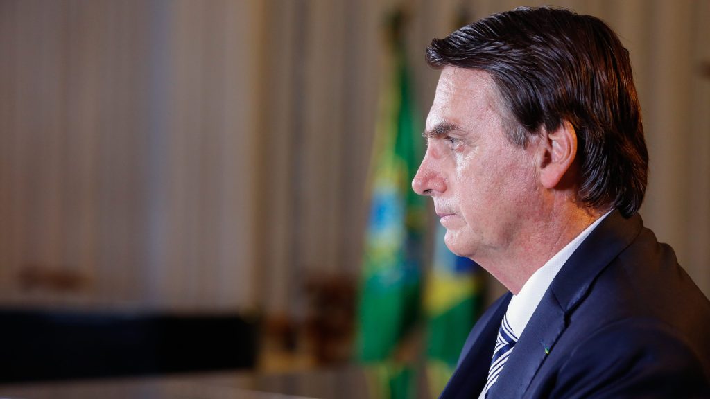 Foto mostra bolsonaro visto de lado, com bandeira do Brasil ao fundo. Julgamento de Bolsonaro será retomado nesta terça (27)
