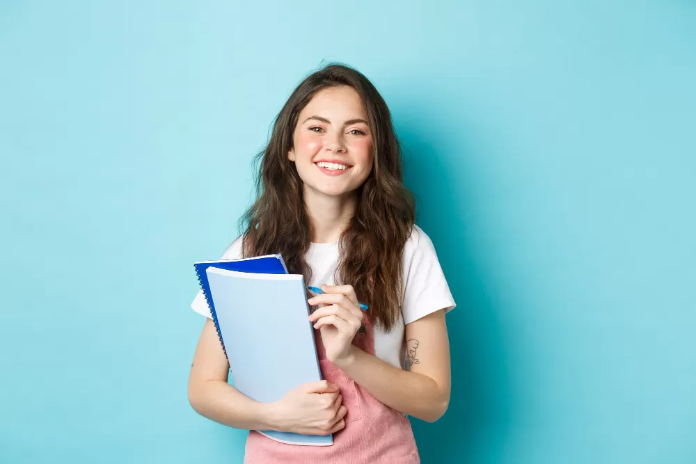 Estudante com livros e caneta na mão, sorrindo. Agência de estágios de SJC está com vagas para administração, Ensino Médio e outras áreas
