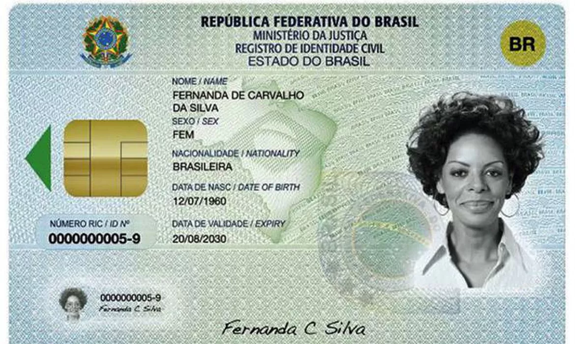 Nova carteira de identidade nacional. Ela apresenta a cor azul claro nas laterais, que em direção ao meio vão se transformando em verde claro com um degradê. Sobre o verde há ainda a marca d'água de um selo da República Federativa do Brasil e um mapa do Brasil com a parte interna da bandeira nacional dentro dele. A carteira apresenta, na parte de cima e ao centro, os dizeres "República Federativa do brasil", "Ministério da Justiça", Registro de identidade Civil e "Estado do Brasil". Abaixo disso, ainda ao centro, há as seguintes informações em sequência vertical: nome, sexo, nacionalidade, data de nascimento e data de validade. Agora na parte esquerda da carteira, há um chip dourado com uma seta verde apontando para a esquerda e abaixo dele está o número da identidade. O mesmo número aparece em uma versão um pouco menor um pouco mais abaixo, no lado inferior esquerdo, junto de uma miniatura da foto da carteira. No lado esquerdo do documento, por sua vez, há a foto de identificação em preto e branco e acima dela, no canto superior direito, um selo amarelo circular com o escrito "BR" na cor preta dentro dele. Por fim, também no centro da carteira, mas na parte inferior, há a assinatura do nome do cidadão.