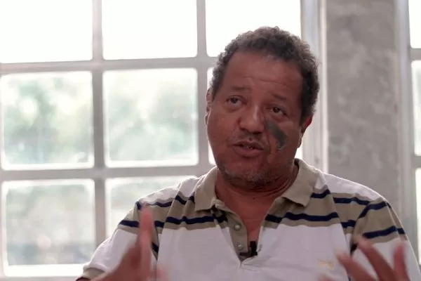 Candidato Luiz Carlos Prates. Ele é pardo, possui cabelo crespo, barba por fazer e mancha de nascença no lado esquerdo do rosto.