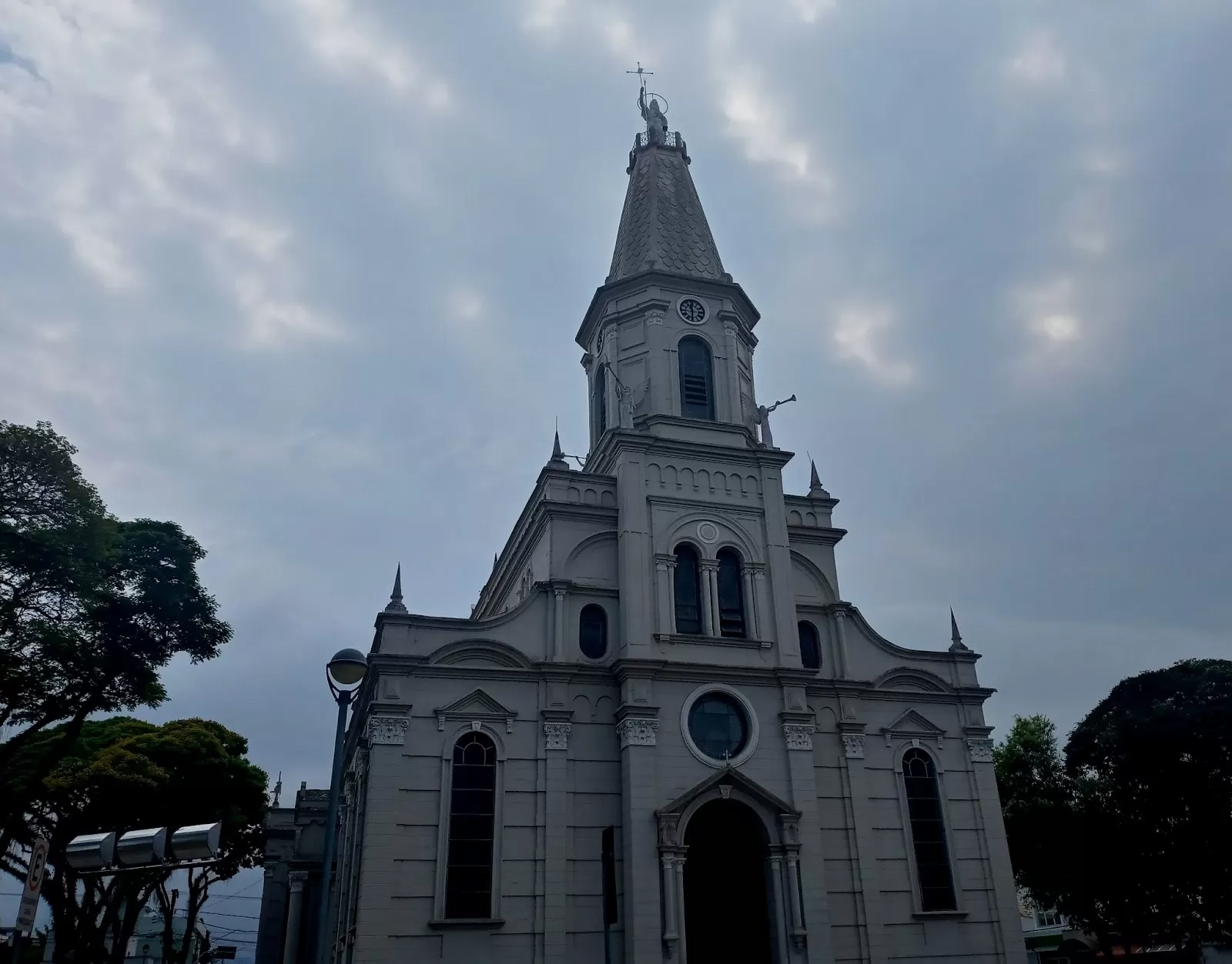 Fachada da Igreja Matriz de São João Batista, um dos pontos turísticos de Caçapava, com um céu azul, árvores na laterais e a fachada branca em destaque, vista de baixo para cima.