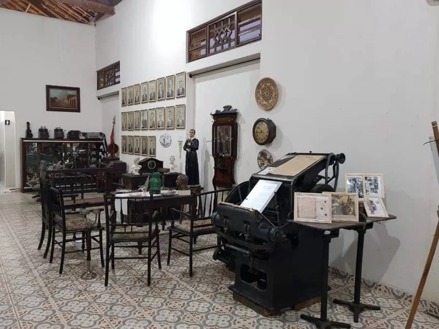 Parte interna do Museu José de Moura Resende, em Caçapava, com um chão de piso, parede branca e móveis antigos, em diversas cores.