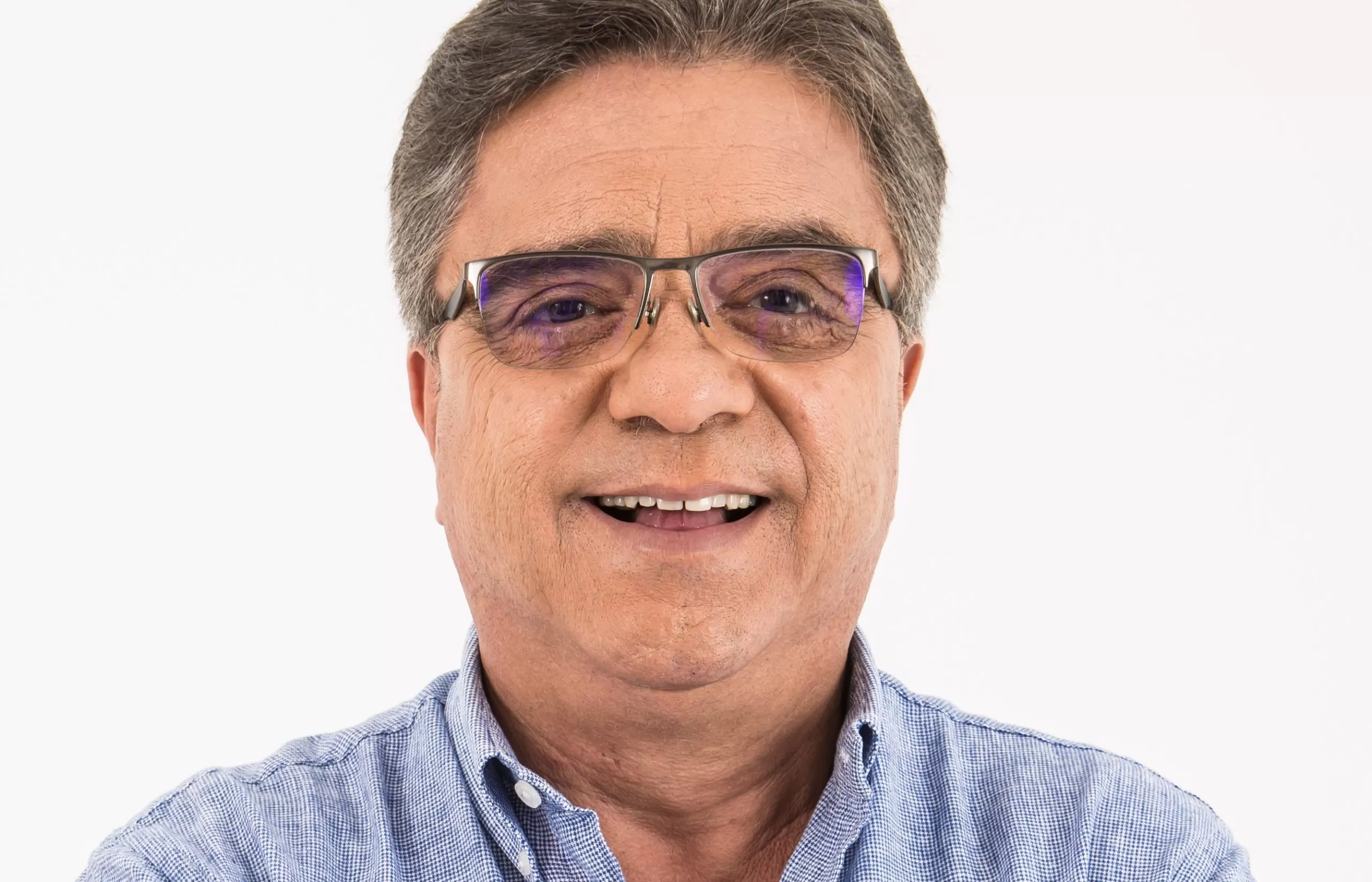 Antônio Carlos da Silva, candidato a deputado estadual por Caraguatatuba, posando sorrindo para foto. Ele aparece do pescoço para cima, é idoso, branco, tem cabelo grisalho penteado para trás e usa óculos e camisa social azul clara.