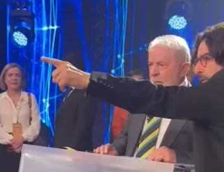 Vídeo mostra Lula xingando o fotógrafo Stuckert durante o debate na Band. Na foto, o assessor aponta para frente, Lula ao lado observa, em um fundo azul.
