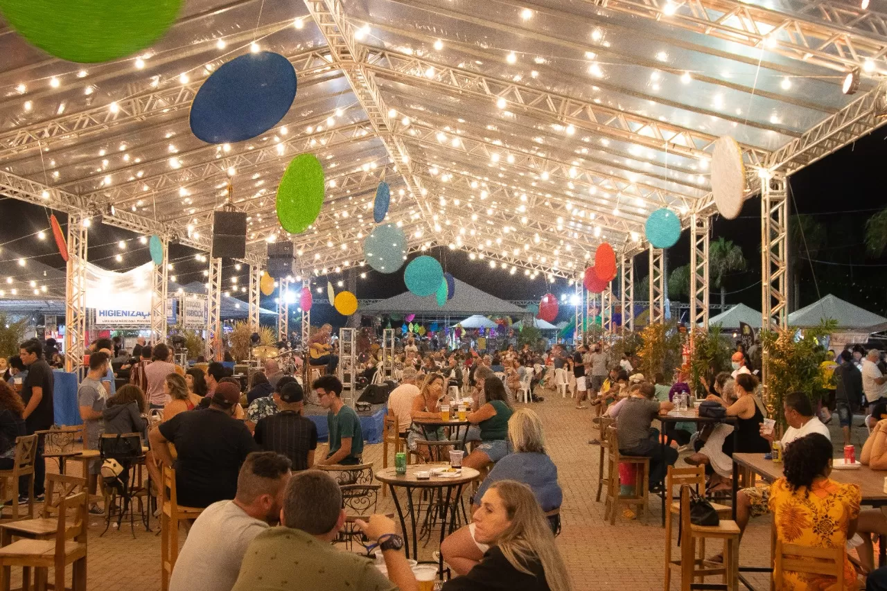 Foto mostra o espaço do Festival Comida de Boteco de São Sebastião, com mesas, iluminação, decoração e pessoas.