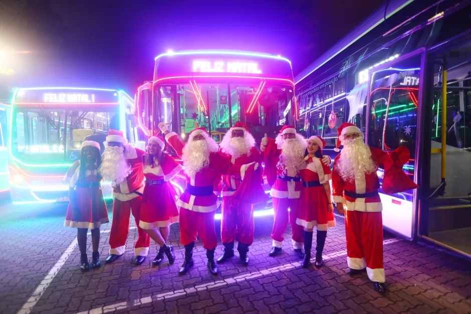 Caravanas de Natal em SJC, com Papais Noel na frente de ônibus iluminados.
