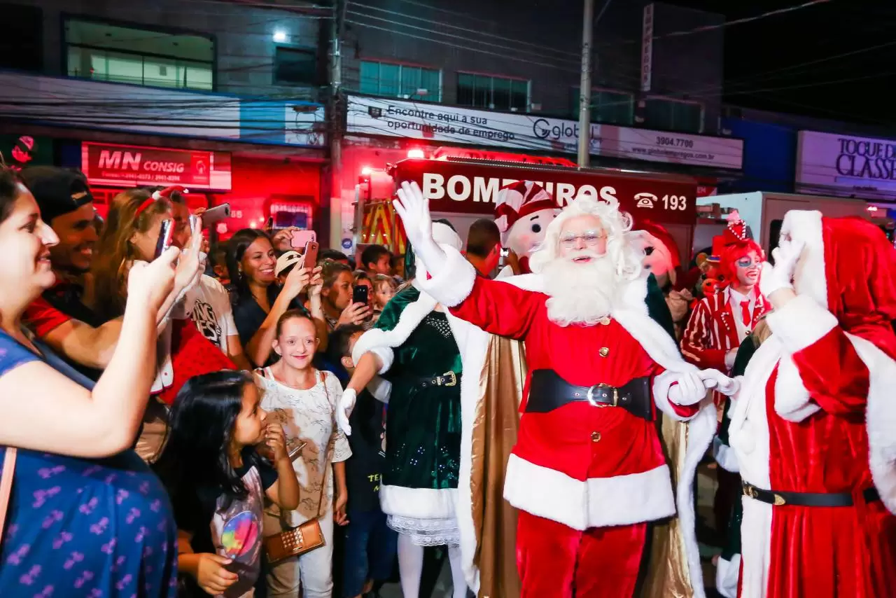 Natal Iluminado de SJC, realizado pela ACI, Prefeitura e FCCR; foto mostra dois Papai Noel com vestimentas vermelhas, e pessoas em volta.