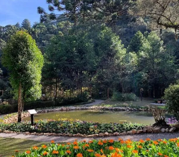 imagem de um bosque, com lago e árvores em volta, flores bem coloridas; foto ilustra a matéria de parques para curtir em Campos do Jordão.