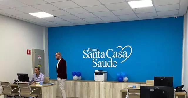 imagem de uma clínica da Santa Casa, com parede azul, e duas pessoas (uma em pé e outra sentada).