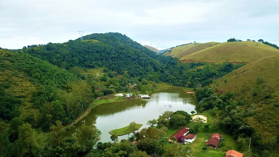 Vista aérea do Vale dos Sonhos, um dos pesqueiros em SJC; foto mostra montanhas de árvores e um lago no Centro, com casas de tijolo na parte direita inferior.
