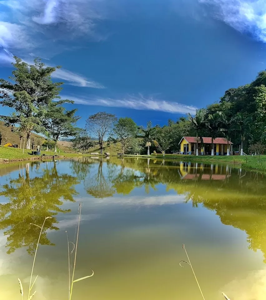 Fachada de um dos Pesqueiros em SJC, o Pesque e Pague do Pedrão, com céu azul, lago, árvores ao redor e uma casa ao fundo.