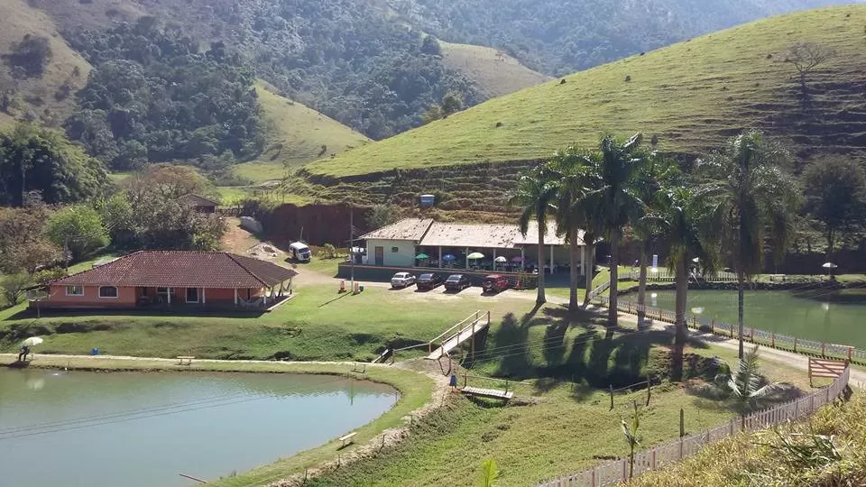 Vista aérea do Pesqueiro & Pousada Bela Vista, com montanhas, árvores, lago e casa; foto ilustra matéria sobre pesqueiros em SJC.