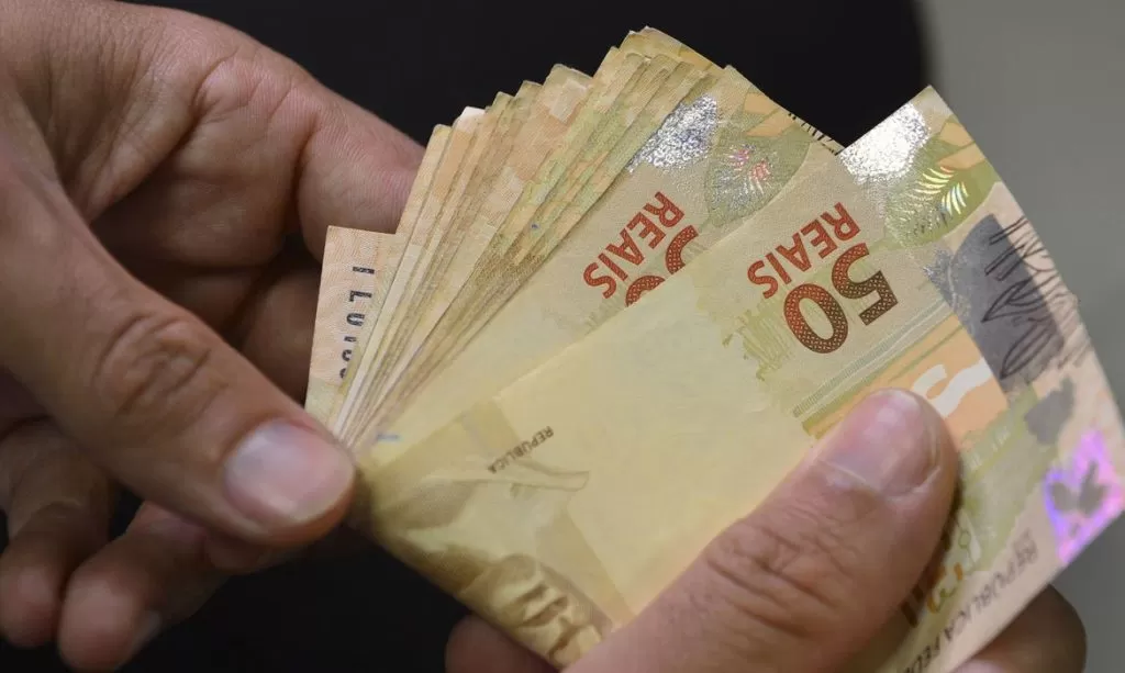 imagem de uma pessoa com noras de 50 reais na mão; foto ilustra matéria sobre saques do dinheiro esquecido começam em 7 de março, informa Banco Central