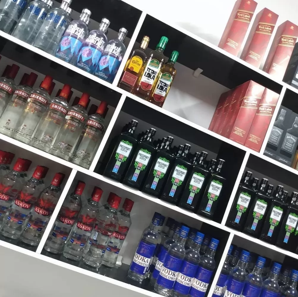 Mais uma opção de adega na zona sul de São José dos Campos, a Madrugadão Sul; foto mostra uma prateleira branca com diversas bebidas apoiadas, incluindo whisky, vodka e outras bebidas.