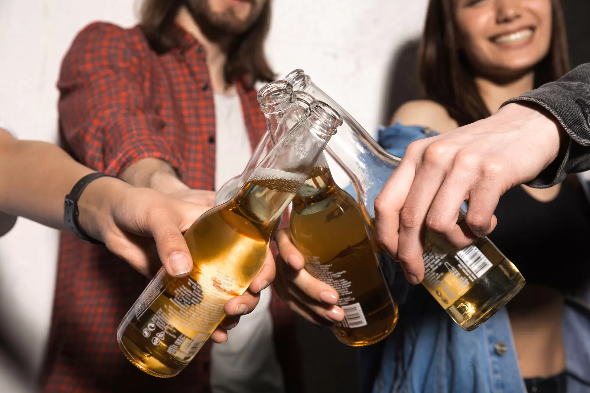 Diversas pessoas, entre homens e mulheres, fazendo um brinde com uma garrafa de cerveja transparente; foto ilustra matéria sobre adegas em São José dos Campos.