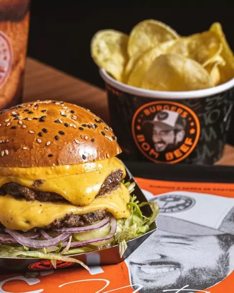 Uma das opções no Bom Beef Burgers, em São José dos Campos, com um lanche no lado esquerdo, com cheddar, pão e alface; ao lado direita há um pote de batata frita; foto ilustra matéria sobre hamburguer artesanal em SJC.