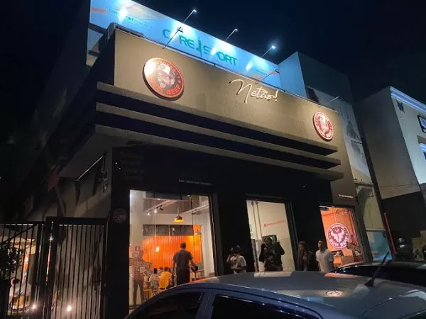 Fachada do Bom Beef Burgers, localizado em São José dos Campos, com uma fachada preta, fosca, com o logo vermelho em cima, carros estacionados em baixo e pessoas entrando no estabelecimento.