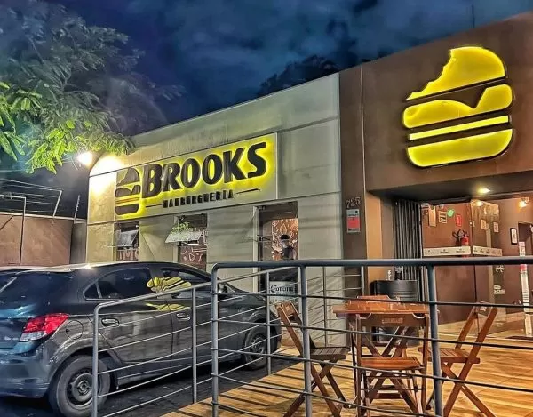 Fachada da hamburgueria Brooks, em São José dos Campos, com uma placa em amarela, iluminada, um carro estacionado à esquerda e a entrada à direita, em madeira.