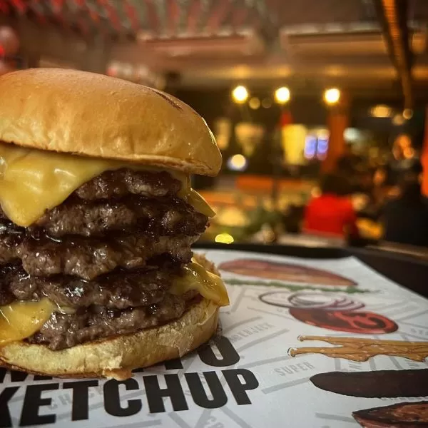 Lanche artesanal com hamburguer, pão, queijo e a decoração do Bullguer ao fundo; foto ilustra matéria sobre hamburgueria artesanal em SJC.