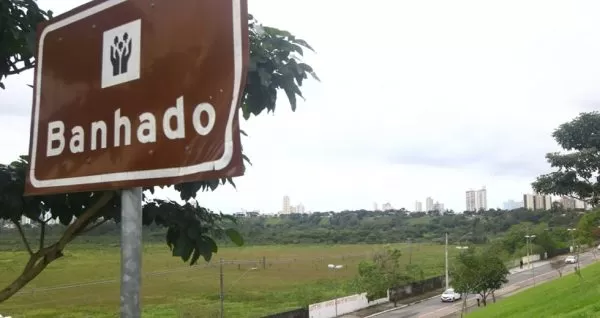Placa do Banhado, com área verde ao fundo, céu azul e carros passando; foto ilustra matéria sobre a decisão da Justiça sobre regularização do bairro Parque Nova Esperança.