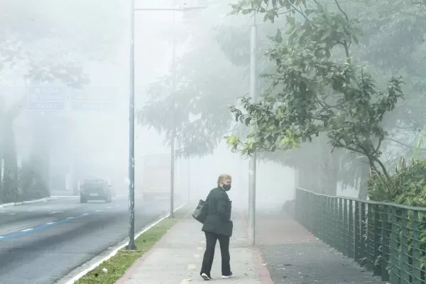 idosa caminhando em calçada em são josé dos campos durante manhã de inverno com bastante nevoeiro; neste ano o inverno no brasil não deve ser tão rigoroso