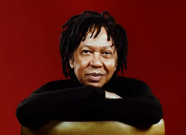 Cantor Djavan sentado em cadeira virada ao contrário apoiando o braço em encosto