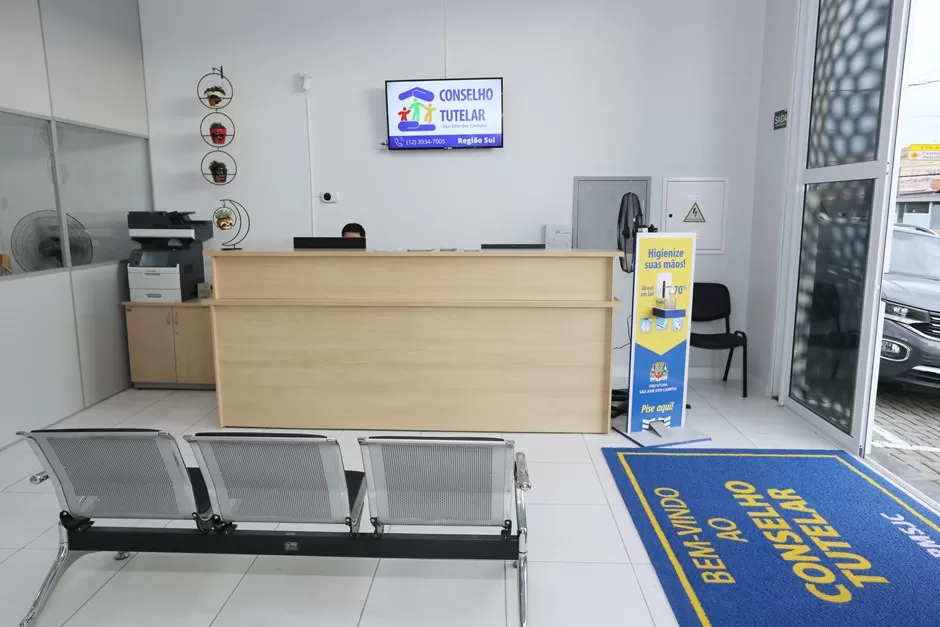 Sala de recepção do Conselho Tutelar da zona sul de SJC com balcão, atendente no computador e cadeiras para espera; órgão terá eleição