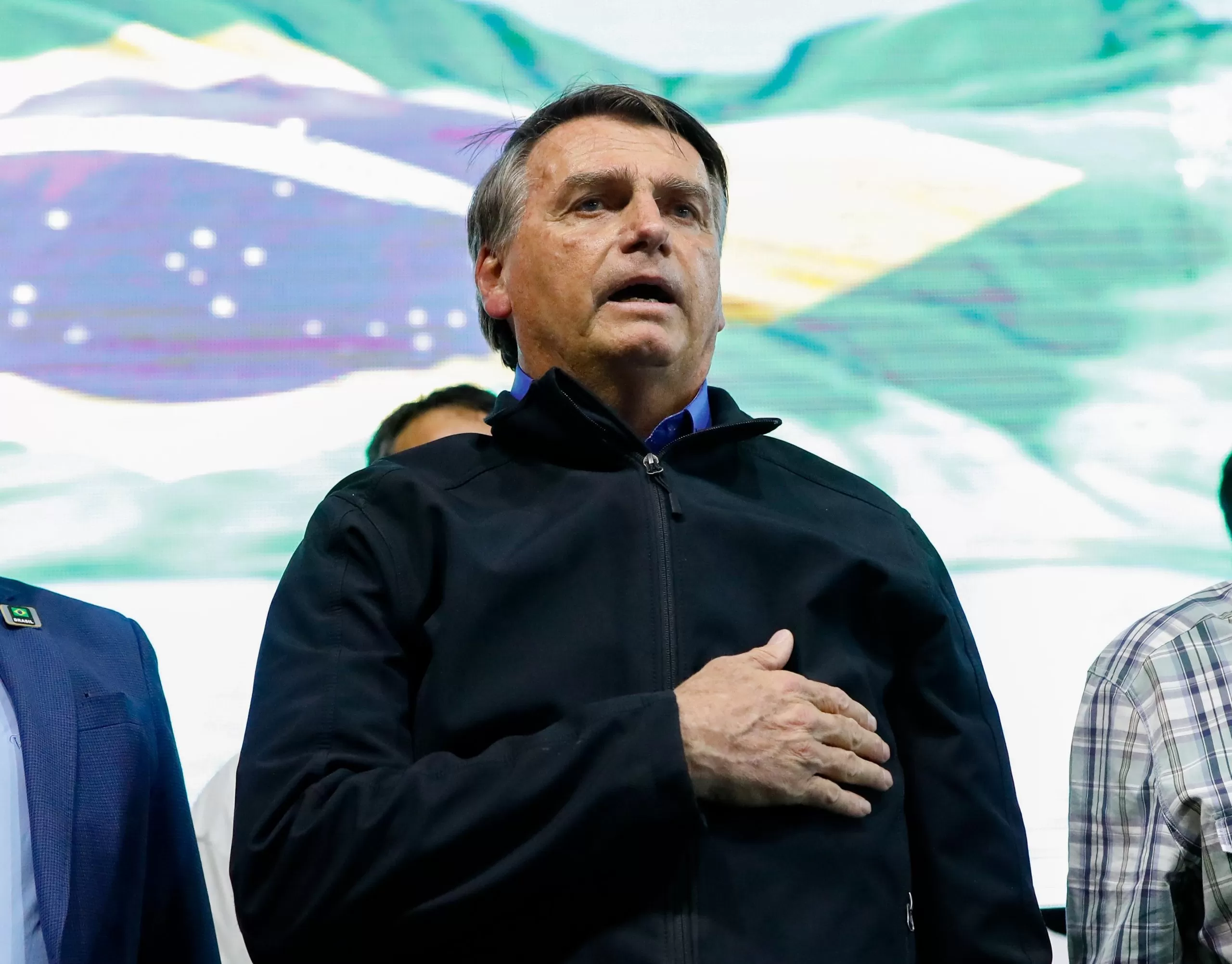 bolsonaro posicionado enquanto ento =a o hino nacional com a mão sobre o peito