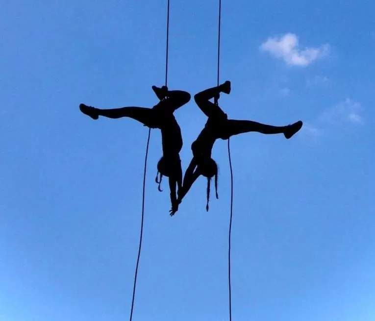 Momento de dança vertical, na qual duas mulheres estão de cabeça para baixo, de braços dados. Esta atividade é feita por uma das professoras dos workshops em são josé