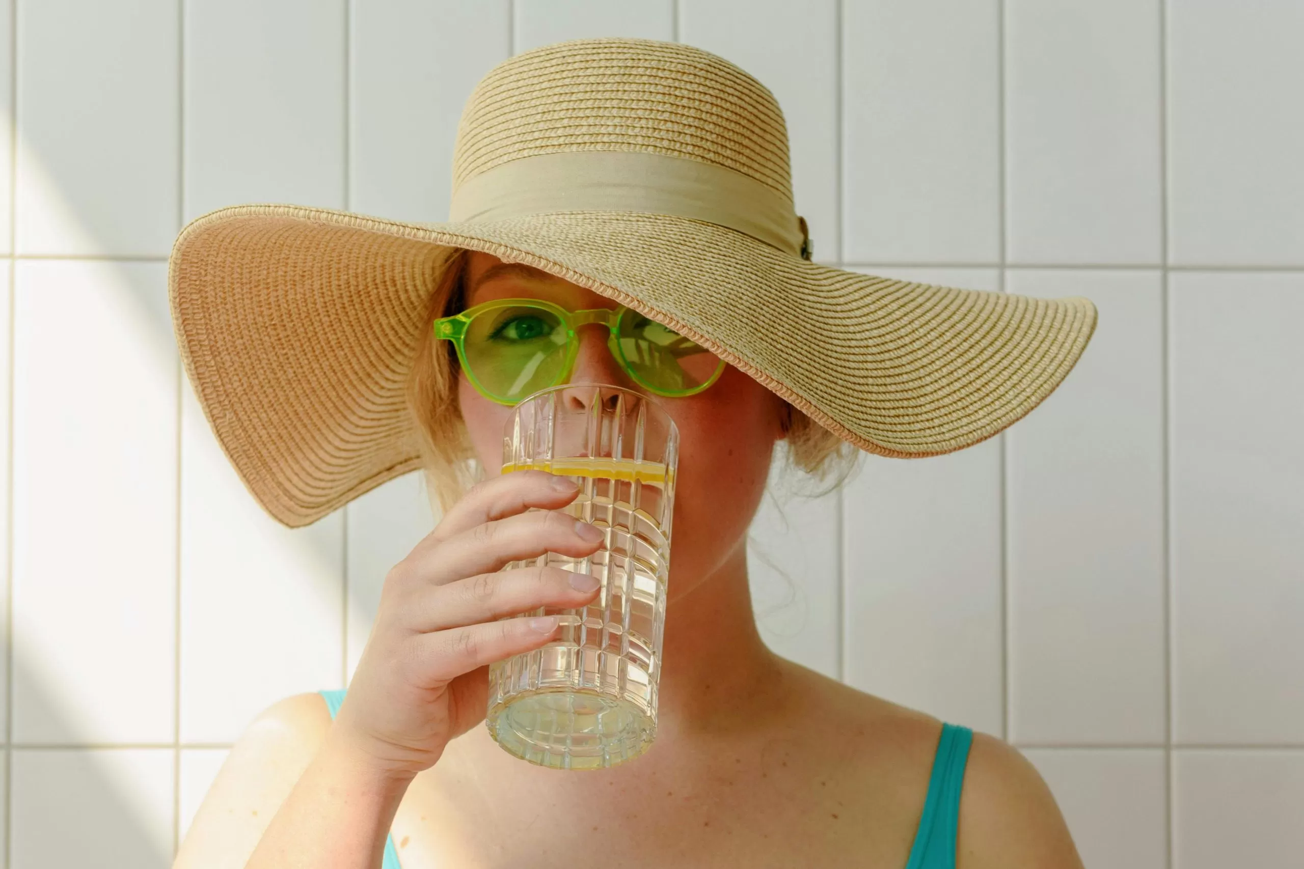 Mulher de chapéu e óculos, tomando água, algumas medidas essenciais para enfrentar a onda de calor no Vale do Paraíba