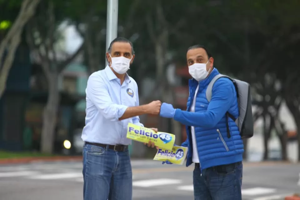 cury e felicio na época da pandemia, de máscara, em rua dando soquinho e com materiais de campanha para a candidatura de felicio a prefeito de são josé dos campos