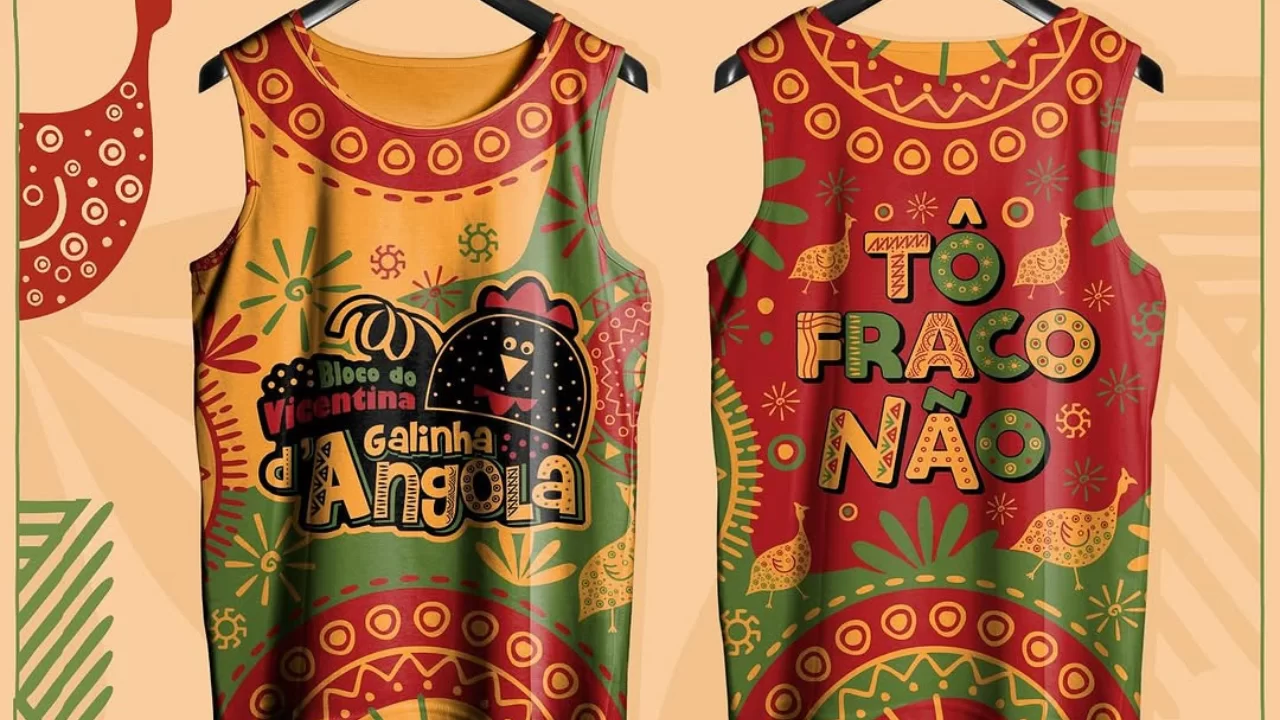 abadá oficial do Bloco Galinha d’Angola 2025 com ilustração de uma galinha-d’angola na frente, rodeada por padrões vibrantes em amarelo, verde e vermelho. No verso, a frase “Tô Fraco Não” se destaca entre elementos gráficos coloridos e geométricos, em um design alegre e vibrante.